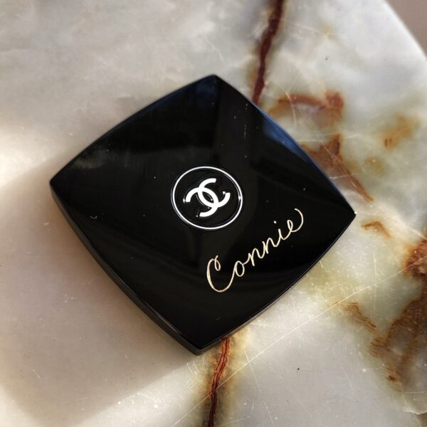 the front of a Chanel compact mirror hand engraved with a name in calligraphy